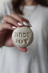 Handmade ceramic stone engraved with Joy (שמחה) in Hebrew and English – a unique decorative or gift item