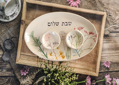 A handmade ceramic Shabbat candle holder set with one-of-a-kind floral impressions and the words "Shabbat Shalom" in Hebrew