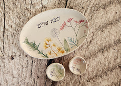 A handmade ceramic Shabbat candle holder set with one-of-a-kind floral impressions and the words "Shabbat Shalom" in Hebrew